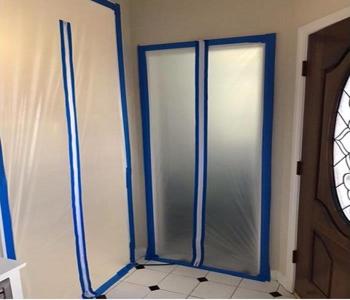 Same bathroom area with the same checkered style flooring but with plastic containment covering the doorway with blue tape. 