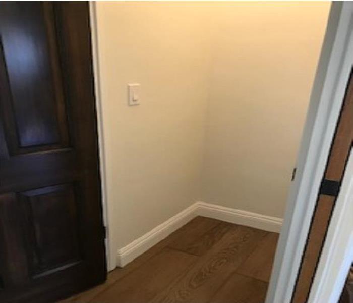 Hallway closet with a dark stained door and medium colored wood flooring with 2 air movers and 1 dehumidifier. 
