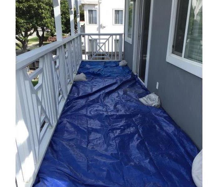 Blue tarp with sand bags is covering the balcony floor. 