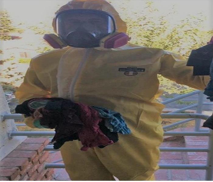 Technician fully clothed in a PPE and full mask, holding dirty rags to clean biohazard 